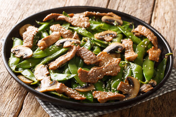 Tasty fried meat with mushrooms and pea pods, garlic, sesame seeds close-up in a plate on the table. horizontal