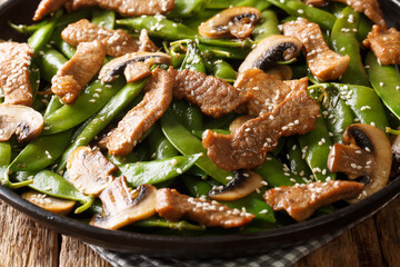 Asian stir-fried beef with mushrooms champignons and pods of green peas, sesame seeds close-up in a plate. horizontal