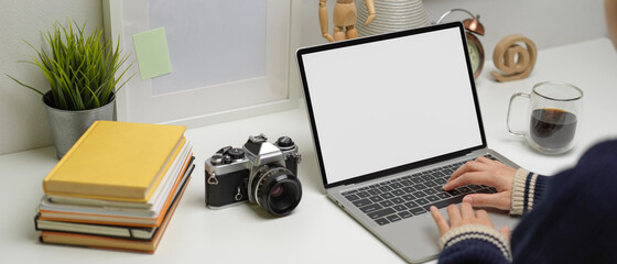 Female freelancer typing on mock-up laptop on home office desk with books, camera and decorations