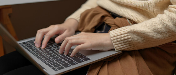 Female hands typing on laptop on her lap while sitting on office chair in office room