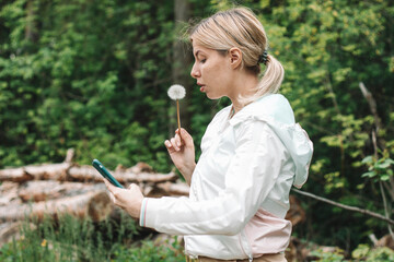 girl is blows away dandelion blowball and doing selfi on phone