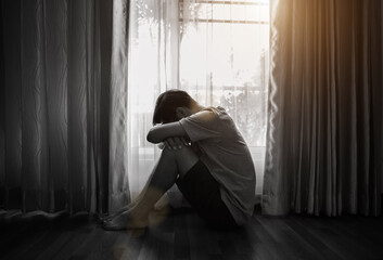 Sad and depressed young male sitting on the floor in the living room looking outside the doors,sad...