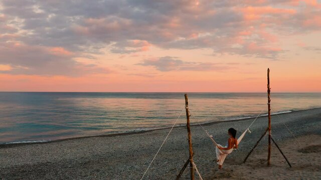 Giovane ragazza si dondola nell'altalena in riva al mare con un tramonto rosso infuocato.