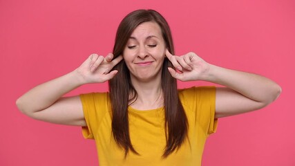 Fun young woman in yellow t-shirt posing isolated on pink background studio. People sincere emotions lifestyle concept. Looking at camera covering ears with hands say blah blah bla do not wanna listen