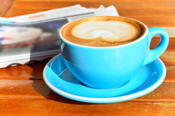 Large cup of morning latte and a newspaper on a wooden table.