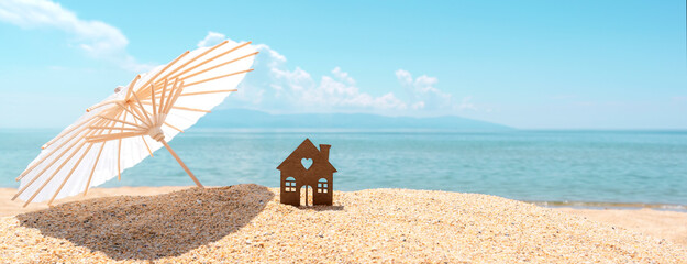 Small house and umbrella on sand, beach, blue sea and sky on blurred background. Real estate, sale...
