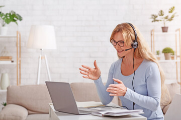 Support and online consultation from home. Woman with headset works remotely at laptop