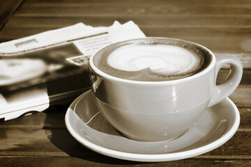 Retro photo of cappuccino and a newspaper. Sepia-toned. Selective focus.