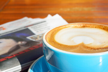 Close-up of cappuccino cup with newpaper in background.