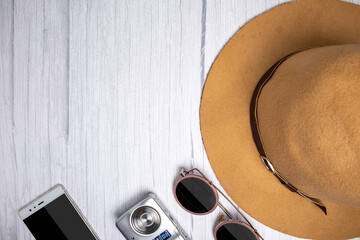 Traveler accessories, luxury hat, sun glasses, camera and smart phone on white white wood background with copy space. Travel vacation concept. Summer background. Flat lay, top view.
