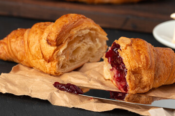Fresh croissants with berry jam on dark wooden board