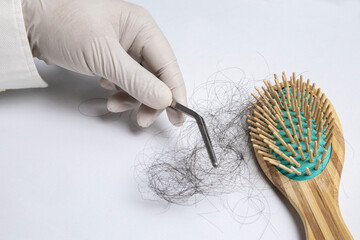 Hair loss experts wear gloves using forceps pick up hair from brush for examination. On a white background with copy space.