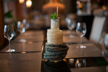 detailed close up drink shot of a delicious fresh mint ice mojito cocktail in a glass bottle covered in jute rope holder standing on a restaurant table on a bokeh blurred background
