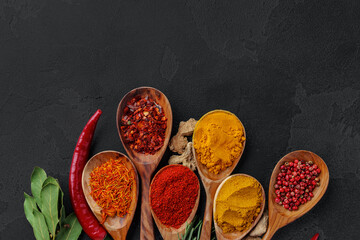 Wooden spoons with various spices on black background