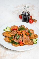 Beef tongue with sauce and vegetables on a white plate