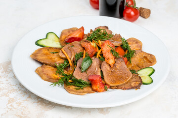 Beef tongue with sauce and vegetables on a white plate