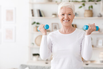 Fototapeta na wymiar Healthy Lifestyle. Positive elderly woman training with dumbbells at home
