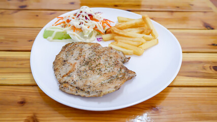 Pork steak with French fries and salad  in a white plate on a wooden table