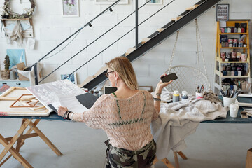 Rear view of busy lady sitting at table and checking contract while working in art studio