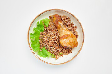 Buckwheat with fried chicken leg on a white plate with a green leaf of salad. Russian traditional cuisine. White background.
