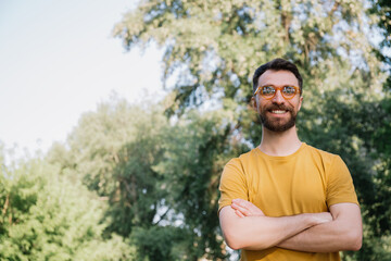 Naklejka na ściany i meble Young smiling bearded man wearing yellow t shirt and stylish eyeglasses, looking at camera standing outdoors