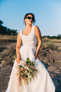 The bride in a luxurious white wedding dress and glasses in nature at sunset