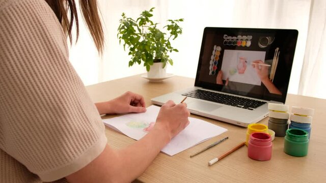 Woman learning to draw on an online course online sitting at home looking over her shoulder. Drawing lesson online on a laptop works on a computer