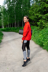 young girl in red jacket with a karemat goes for a training in nature