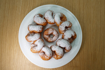 top view of a pile of delicious sweet golden brown doughnuts (donuts) with white powdered icing sugar topping laying in a white plate on a wooden table background