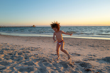 Happy boy kid playing on the beach on summer holidays. Children in nature with beautiful sea, sand and blue sky. Happy kids on vacations at seaside running in the water.