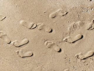 Fototapeta na wymiar Many prints of male feet on the sea sand. Walk barefoot along the shore with footprints. Tourist rest.