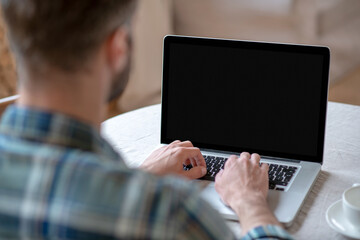Man in a checkered shirt sitting at the table and typing on a laptop