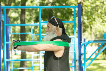 Obraz premium Old man doing fitness exercises with elastic resistance band.Bearded senior training with rubber band. Workout ,sports, healthy lifestyle concept.