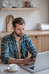 Man in a checkered shirt texting and looking serious
