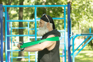Obraz premium Old man doing fitness exercises with elastic resistance band.Bearded senior training with rubber band. Workout ,sports, healthy lifestyle concept.