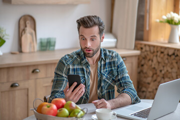 Fototapeta premium Man in a checkered shirt reading a message and looking astonished