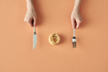 Fettuccine pasta, fork and knife in hands isolated on beige background, minimalistic photography for food blog or ad