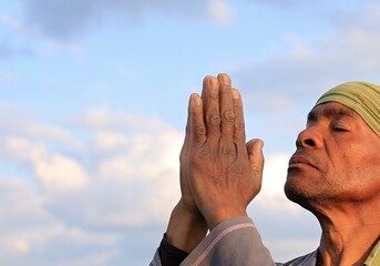 man praying to god with hands together Caribbean man praying with sky background stock photo