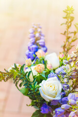 Flower arrangement with white roses, blue delphiniums, and greenary against sunny background