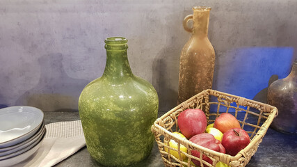 Large glass vases, a basket with apples and plates in the interior of a modern kitchen. The combination of wood and concrete in the design. Modern style dining kitchen