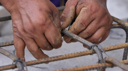 Closeup shot of bar bender hands fixing steel reinforcement bars with binding wire - Powered by Adobe