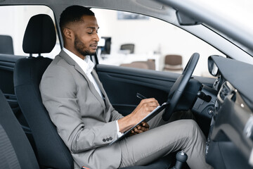 Fototapeta na wymiar Dealer Taking Notes Sitting In Car Checking Automobile In Dealership