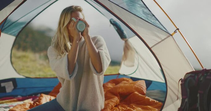 Happy attractive young woman drinking warm tea camping in the mountains, camping adventure lifestyle outdoors