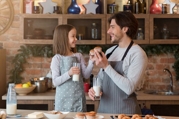 Happy Girl And Her Father Eating Muffins And Drinking Milk In Kitchen