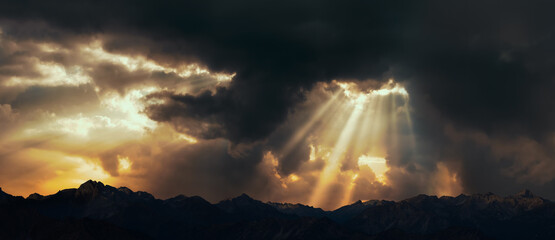 Rays of light shining through dark clouds over mountains. Cinematic scene.