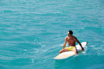 Shot of a handsome young man enjoying a surf in clear blue water, male surfer in the ocean water with surf board, sexy man surfing at the beach, men drifting on surfboard in the copy space ocean