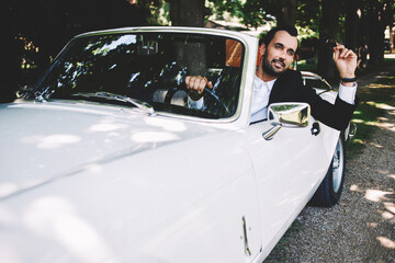 Successful and wealthy businessman sitting behind the wheel of his luxury cabriolet car on countryside road, sure and confident handsome man sits in his new convertible car outdoors looking so happy