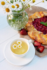 Freshly baked homemade galette or open strawberry pie and fresh mint leaves with a cup of chamomile herbal tea, summer food. Soft selective focus.