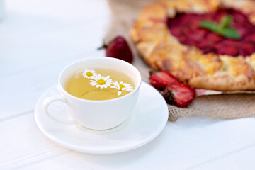 Obraz na płótnie Canvas Freshly baked homemade galette or open strawberry pie and fresh mint leaves with a cup of chamomile herbal tea, summer food. Soft selective focus.