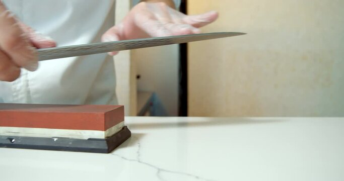 Chef hands sharpening knife in slow motion. Closeup man hands preparing professional tools for cooking food at kitchen restaurant.
